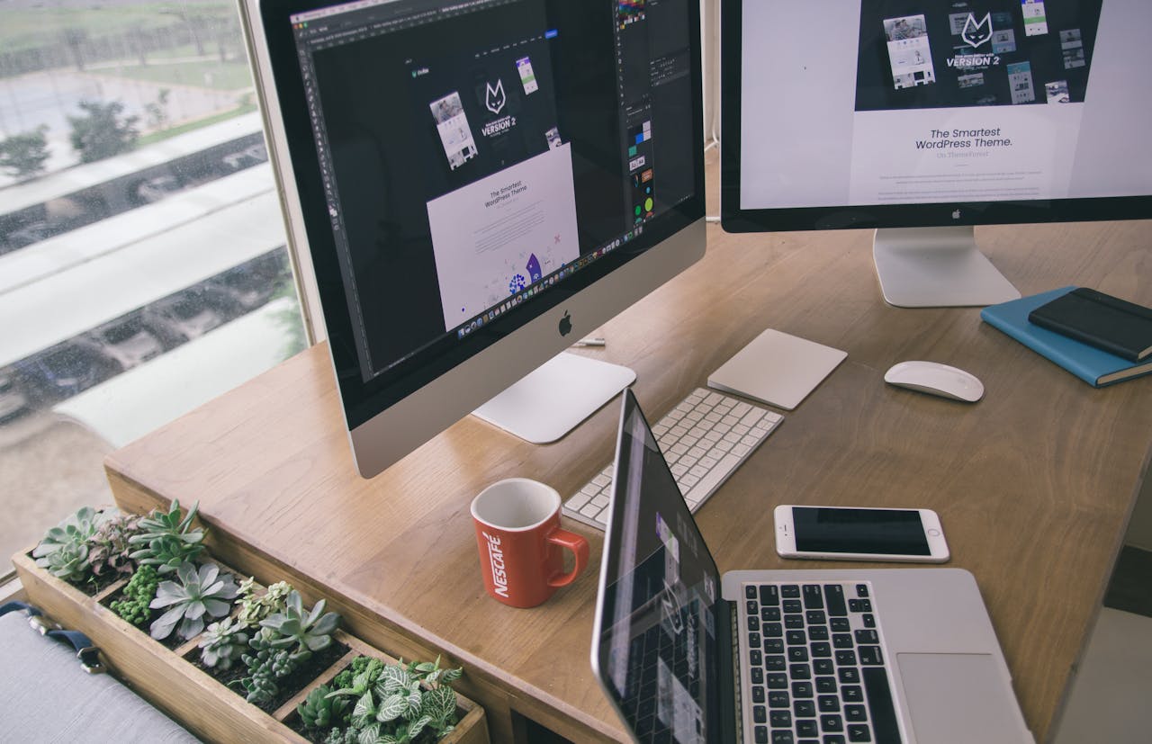Sleek office desk setup featuring Apple computers and greenery for a modern work environment.